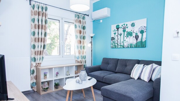 A modern living room with a grey sofa, a white coffee table, and a window with patterned curtains. - Chic apartment in Athens (Athens)