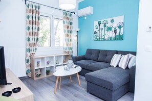Un salon moderne avec un canapé gris, une table basse blanche et une fenêtre agrémentée de rideaux à motifs.
