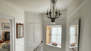 A hallway with a white door, a staircase with a wooden handrail, and a chandelier. - Bell Cliff House (Lyme Regis)