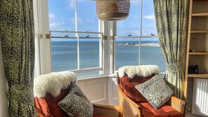 A room with two wicker chairs, a white fur throw, and a view of the sea through a large window. - Bell Cliff House (Lyme Regis)