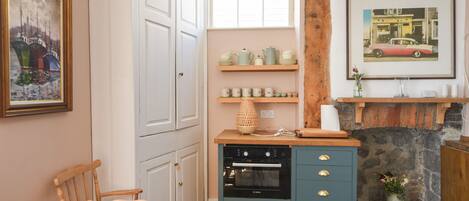 A cozy kitchen with a wooden table, chairs, a Bosch oven, shelves with kitchenware, and a fireplace.