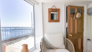 A room with a wicker chair, a white cushion, a wooden door, and a view of the sea through a large window. - Bell Cliff House (Lyme Regis)