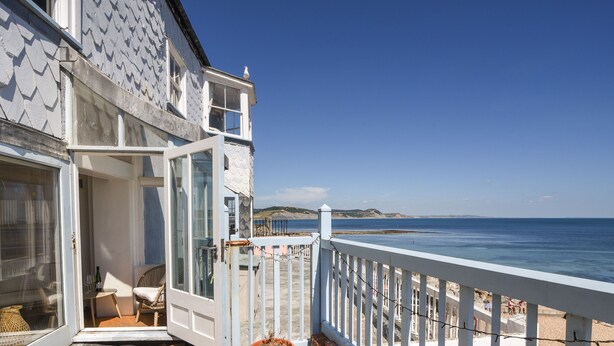 A coastal property with a balcony overlooking the sea, a small outdoor seating area, and a potted plant. - Bell Cliff House (Lyme Regis)