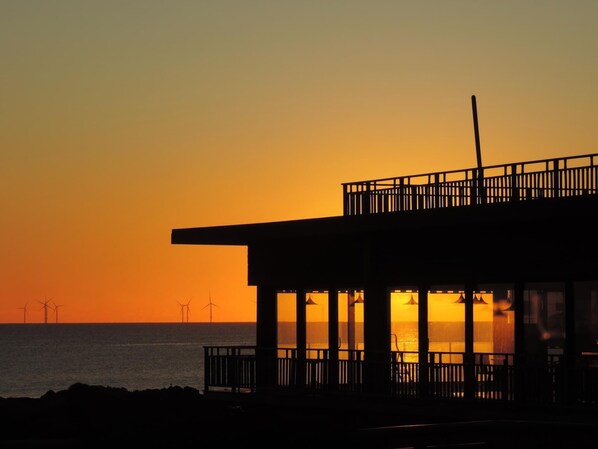 A building with a balcony overlooking the sea at sunset.