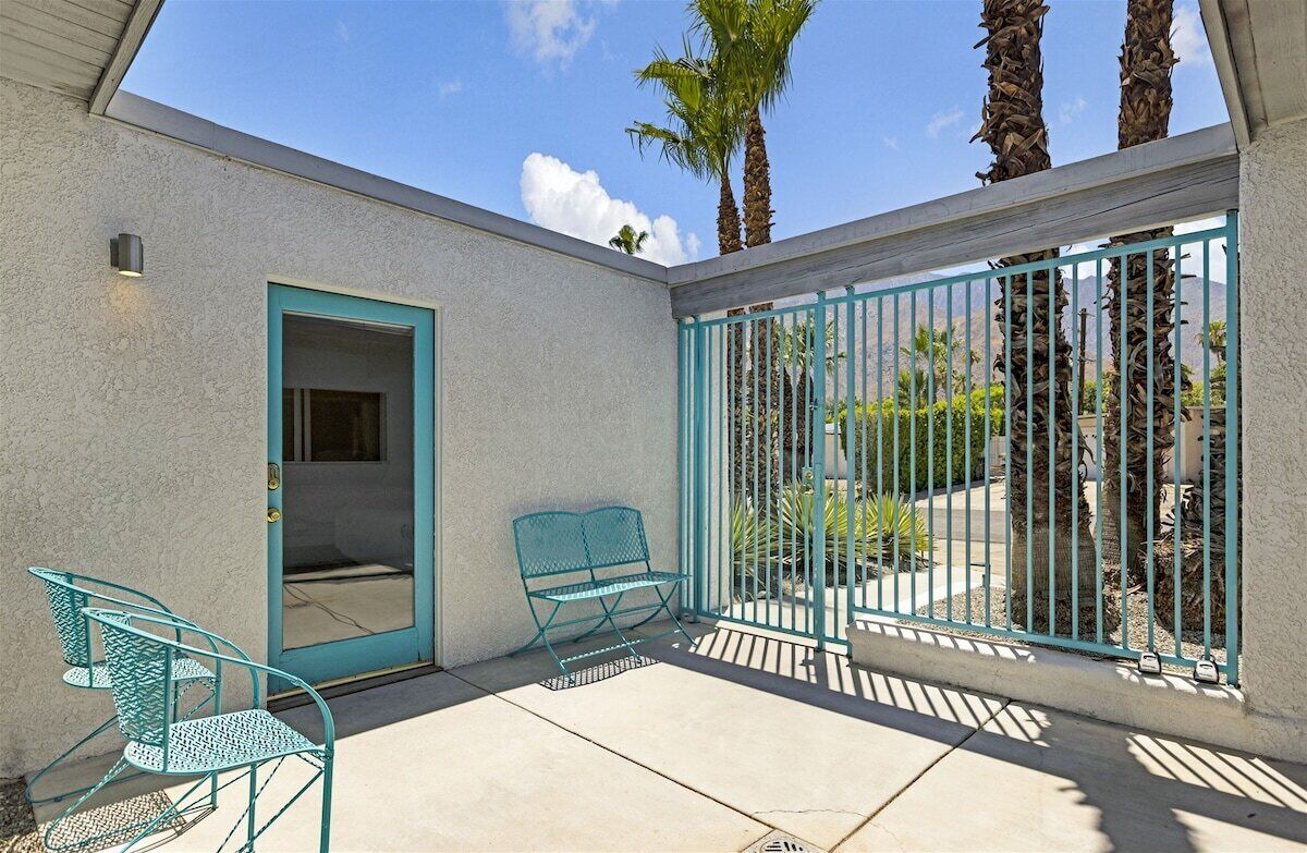 Une terrasse avec un banc et des chaises en métal de couleur turquoise, une porte et un portail en métal.