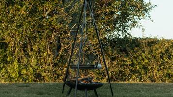 A metal swing set with a fire pit in the middle, surrounded by grass and trees.
