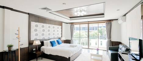 Un dormitorio moderno con una cama grande, un escritorio, una silla, un televisor y un balcón con cortinas.