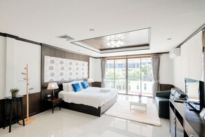 A modern bedroom with a large bed, a desk, a chair, a TV, and a balcony with curtains. - The Panwa House Phuket (Wichit)