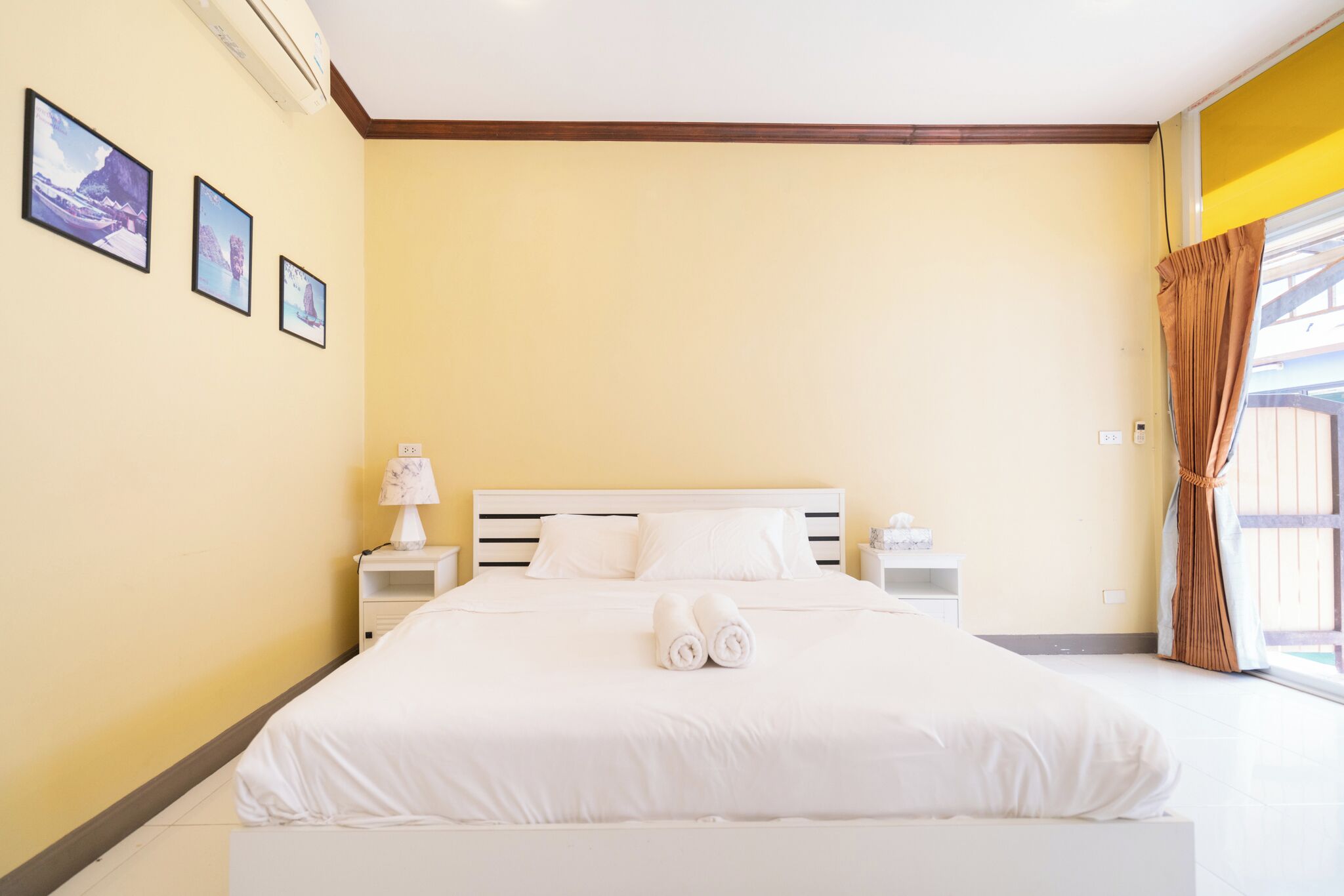 A neatly made bed with white linens and rolled towels, a bedside lamp, and a nightstand with a small decorative item.