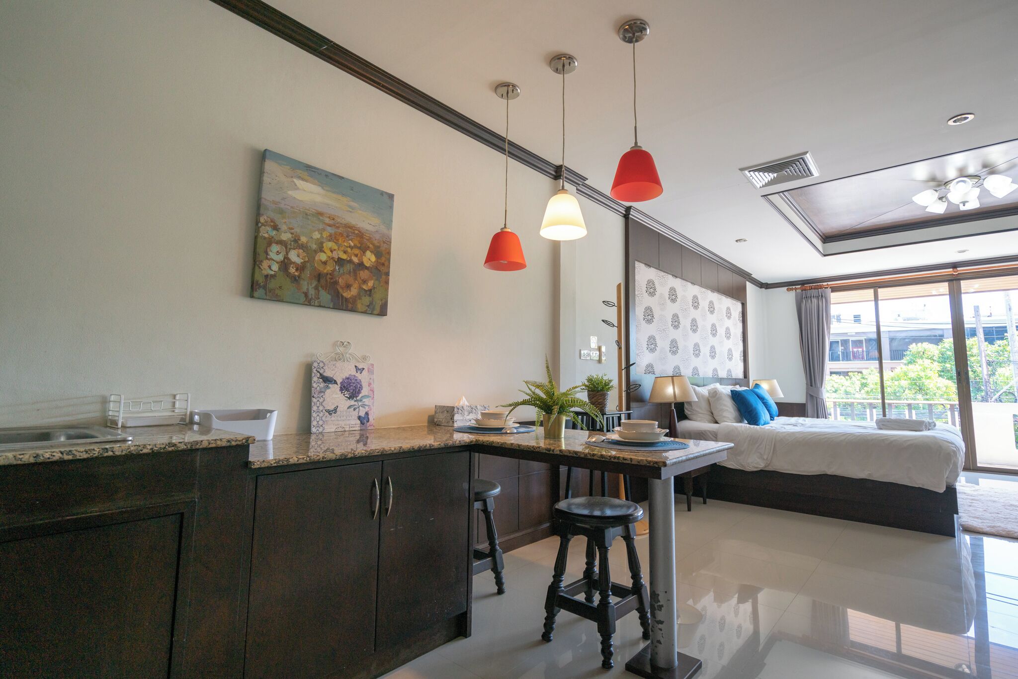 A modern kitchen with dark cabinets, a granite countertop, and a dining area with a table and chairs. There is a painting on the wall and a large window with a view of the outside.