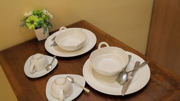 A table set with white dishes, including a teapot, cups, and saucers, with a small potted plant on the side.