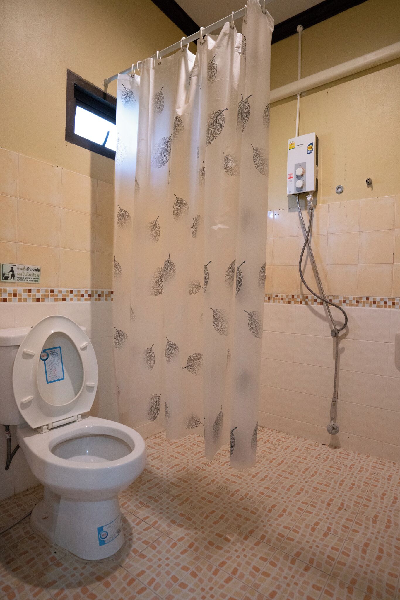 A bathroom with a toilet, a shower, and a curtain with a leaf pattern.