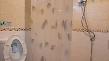 A bathroom with a toilet, a shower, and a curtain with a leaf pattern.