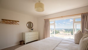 A bedroom with a large bed, a dresser, a mirror, and a window with curtains.