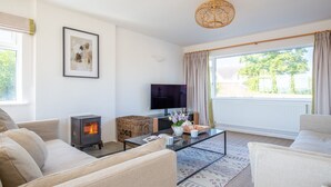 A cozy living room with a fireplace, comfortable seating, a flat-screen TV, and a large window offering a view of greenery. - Ridgeway Farmhouse at Ragley Estate, Alcester - sleeps 8 guests  in 4 bedrooms (Alcester)
