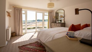 A bedroom with a large bed, a dresser, a mirror, and a view of the outdoors. - Ridgeway Farmhouse at Ragley Estate, Alcester - sleeps 8 guests  in 4 bedrooms (Alcester)