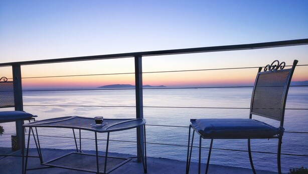 Un balcon avec deux chaises et une table, donnant sur une mer calme et un ciel au coucher du soleil.