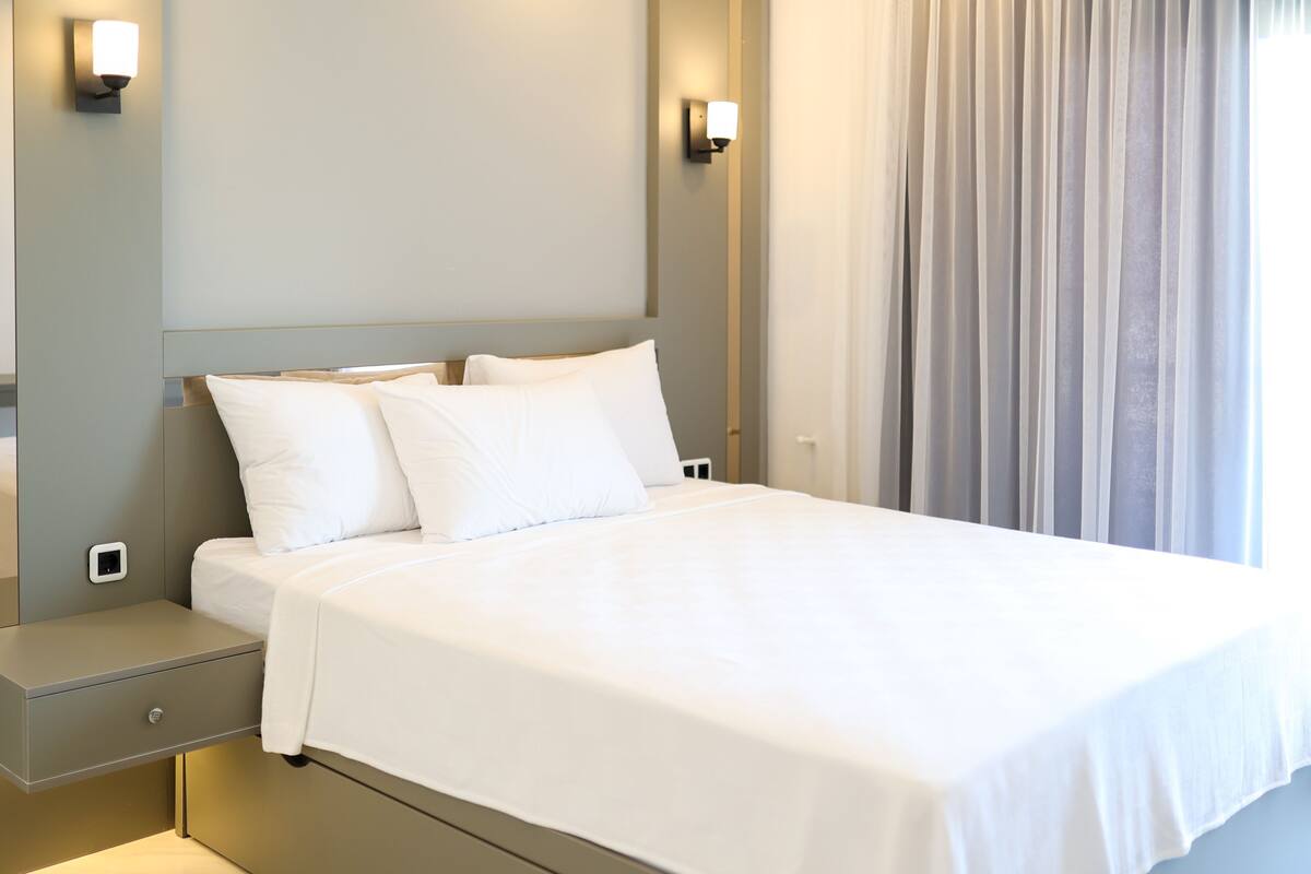 Un lit bien fait, avec du linge de lit blanc, une table de chevet avec une lampe et une fenêtre avec des rideaux.
