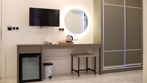 Quarto compacto com cozinha compacta, pequena geladeira, televisão montada sobre um espelho e guarda-roupa de correr.