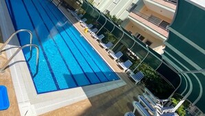 Piscina com espreguiçadeiras e um prédio com varandas.