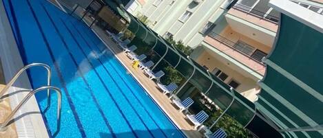 Una piscina con sillas de descanso y un edificio con balcones.