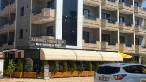 Um edifício de vários andares com varandas, um restaurante e café no nível térreo, e um carro estacionado em frente.