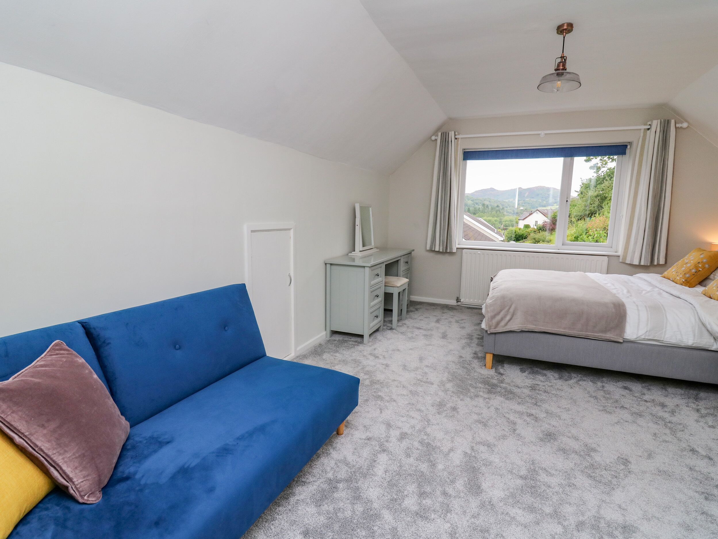 Une chambre avec un canapé bleu, un lit, un bureau et une fenêtre donnant sur un paysage verdoyant.
