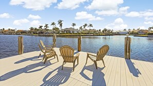 A wooden deck with chairs overlooking a calm body of water, surrounded by houses and palm trees. - Direct Boating Access Home | Pool/Spa & Billiards (Marco Island)