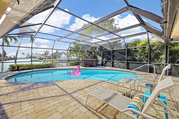 A covered pool area with lounge chairs and a hot tub.