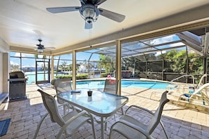 An outdoor patio with a glass-enclosed pool, a ceiling fan, and a table with chairs.