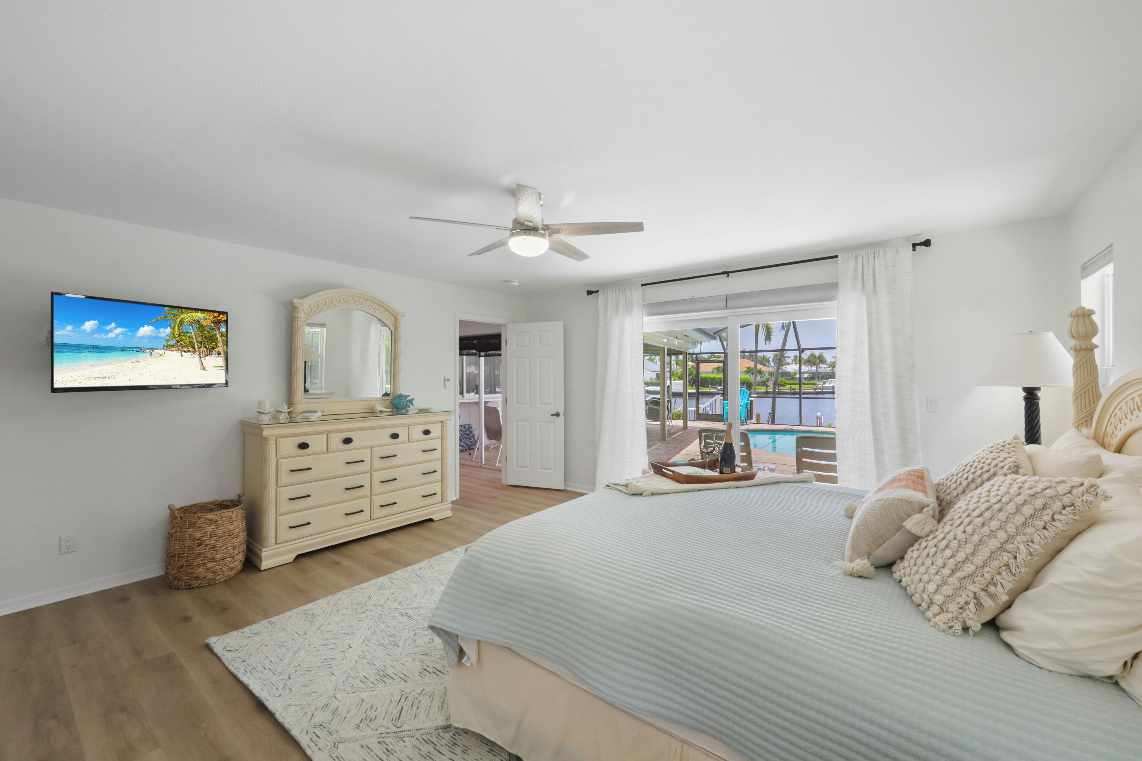 Un dormitorio con cama, cómoda, televisor y vista a una piscina y zona exterior.
