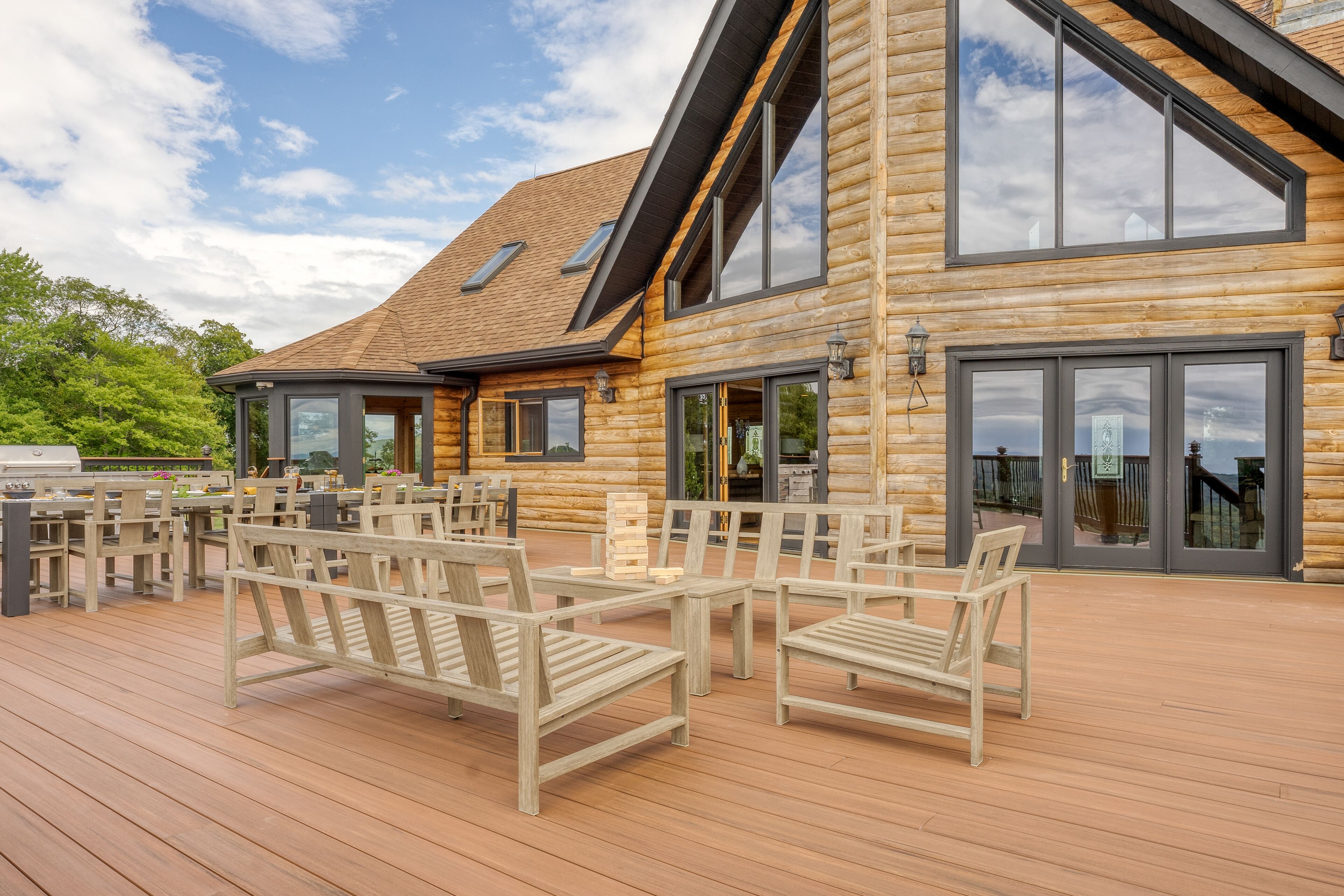 Una cabaña de madera con terraza, asientos exteriores y ventanas amplias.