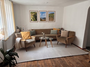 Un salon comprenant un canapé, deux fauteuils, une table basse et une grande fenêtre ornée de rideaux légers.
