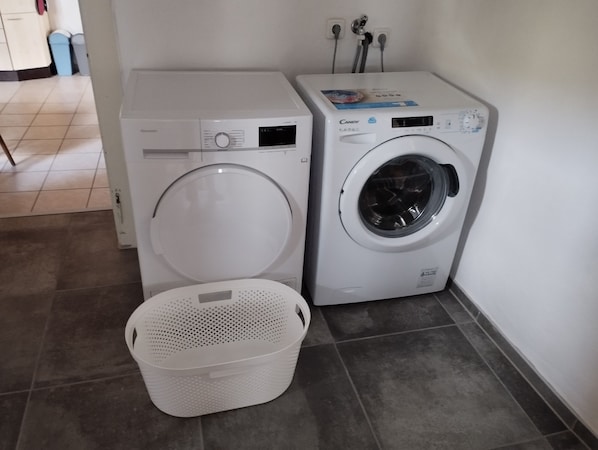 Deux machines à laver à chargement frontal et un panier à linge blanc dans une buanderie.