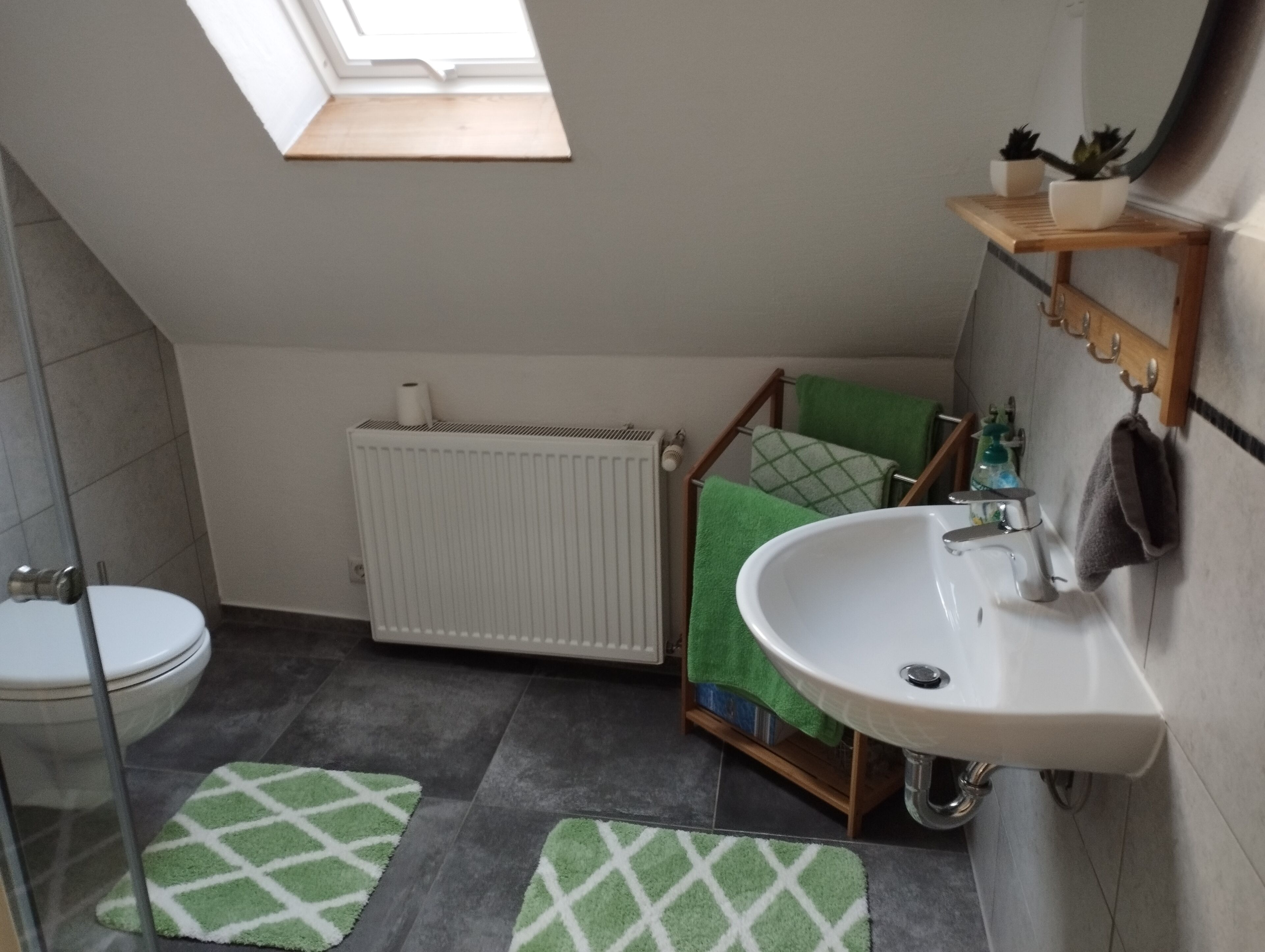Ein kleines Badezimmer mit Oberlicht, einem weißen Heizkörper, einem grünen Handtuch und einem Waschbecken.