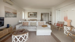 A modern living room with a sofa, coffee table, and chairs, a television, and a dining area in the background. - Apartment 'Cascais Bay Terrace IV' with Sea View & Wi-Fi (Cascais)