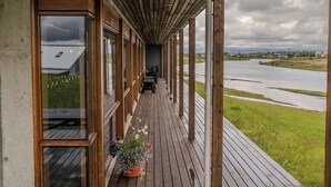 A wooden deck with a view of a river and distant buildings. - West Ranga lodge (Rangárþing ytra)