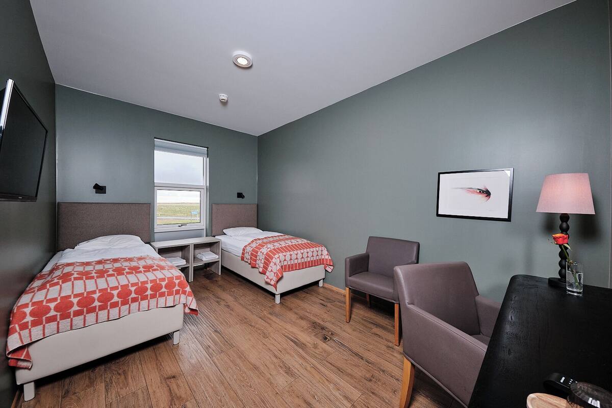 Quarto de hotel com duas camas, uma escrivaninha, uma cadeira, uma televisão e janela com vista.