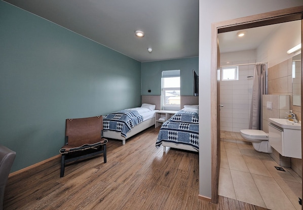 A room with two beds, a chair, a window, and a bathroom visible through an open door.
