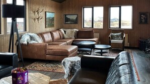 A cozy living room with a brown leather sofa, a round coffee table, and a large window offering a view of the landscape. - West Ranga lodge (Rangárþing ytra)