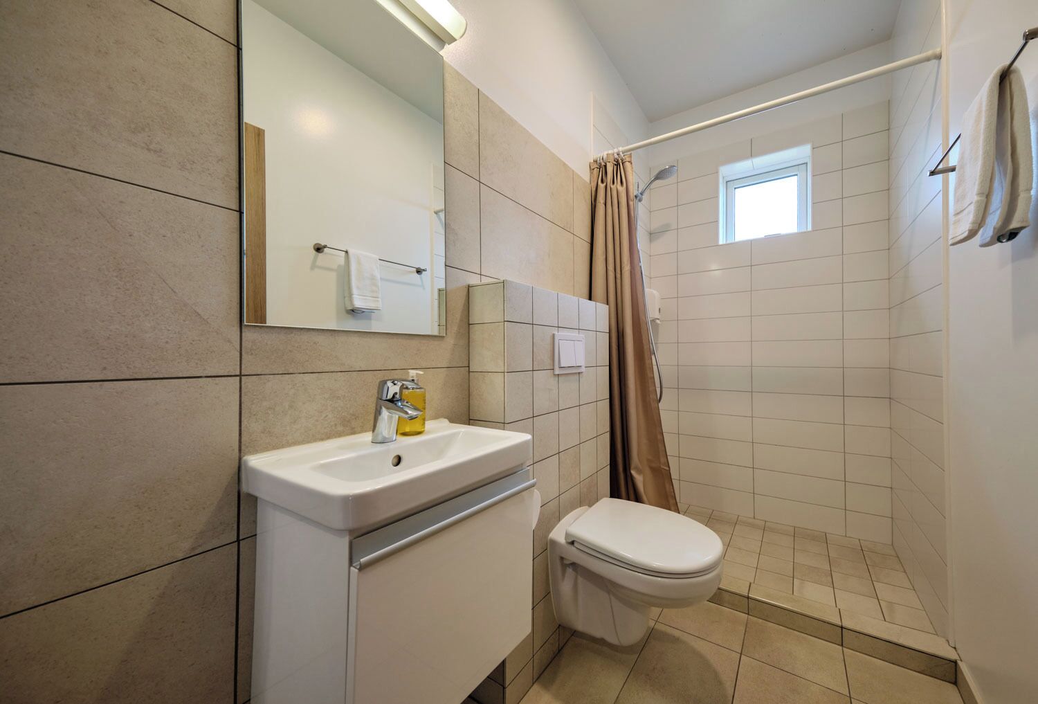 A bathroom with a sink, mirror, toilet, shower, and a window.