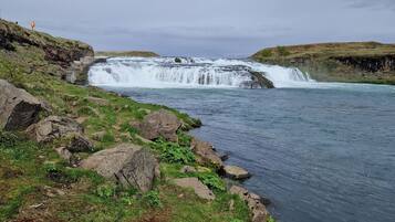 Un paisaje natural con cascada, terreno rocoso y una zona cubierta de hierba.