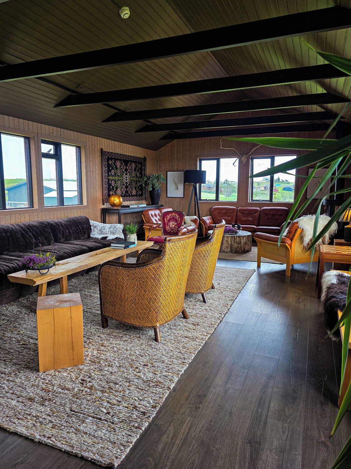 Ein geräumiges Wohnzimmer mit einer großen Couch, mehreren Sesseln, einem Couchtisch und Blick ins Freie durch große Fenster.