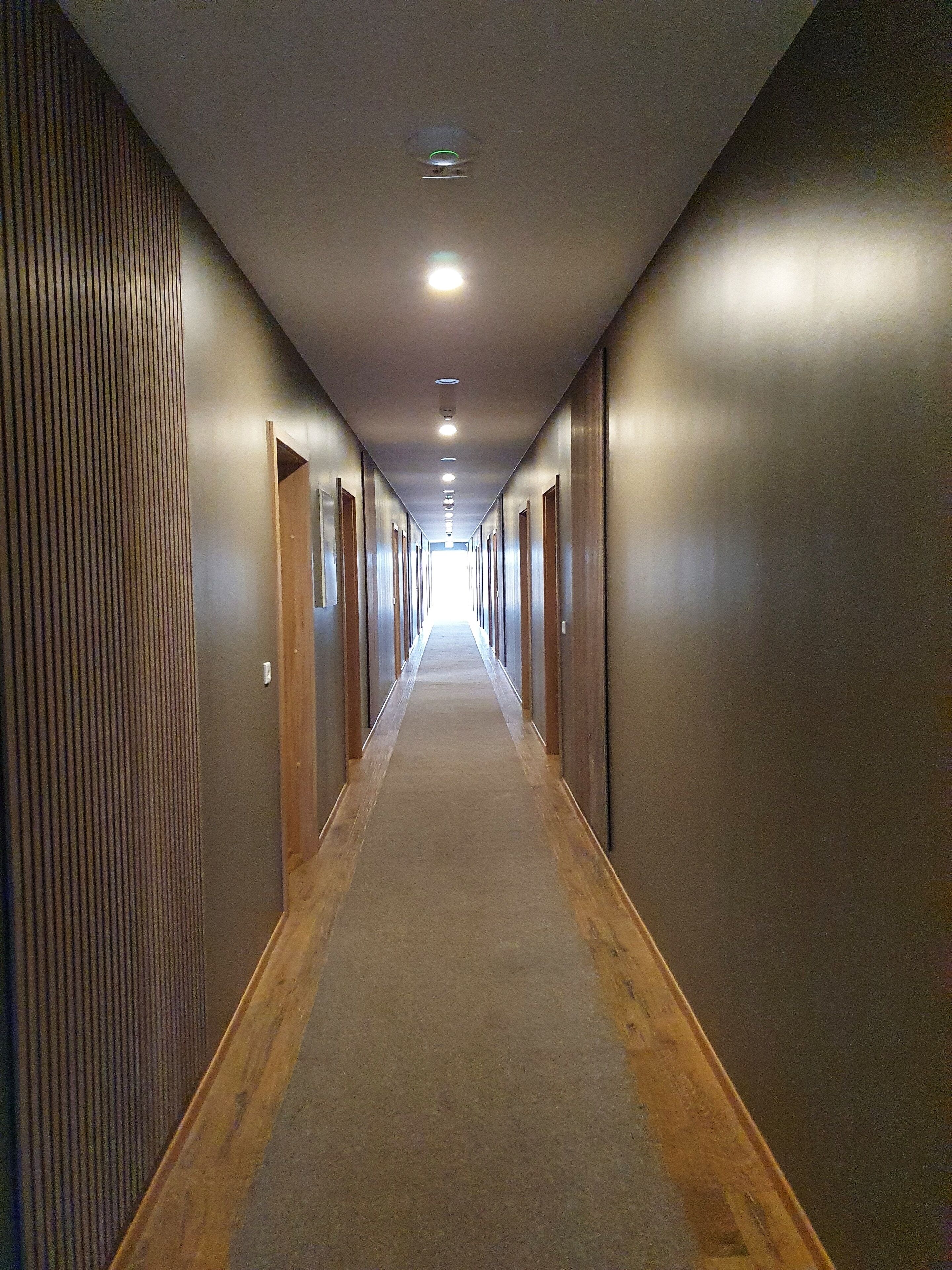 Un pasillo largo y estrecho de hotel con pisos de madera y puertas a ambos lados.