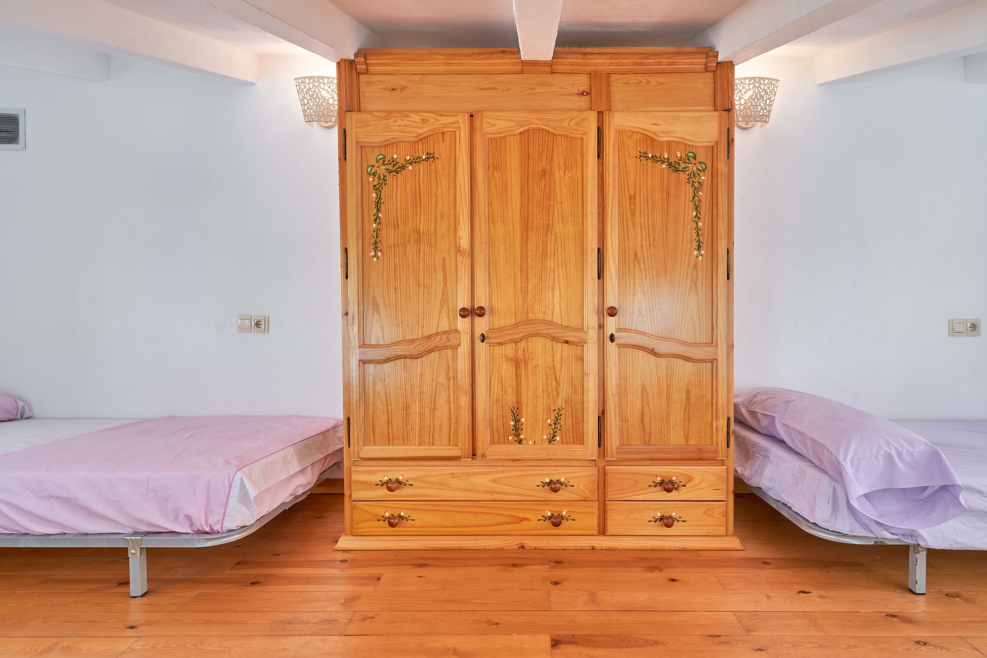 Quarto com guarda-roupa de madeira, duas camas de solteiro e chão de madeira.