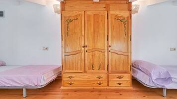 Quarto com guarda-roupa de madeira, duas camas de solteiro e chão de madeira.