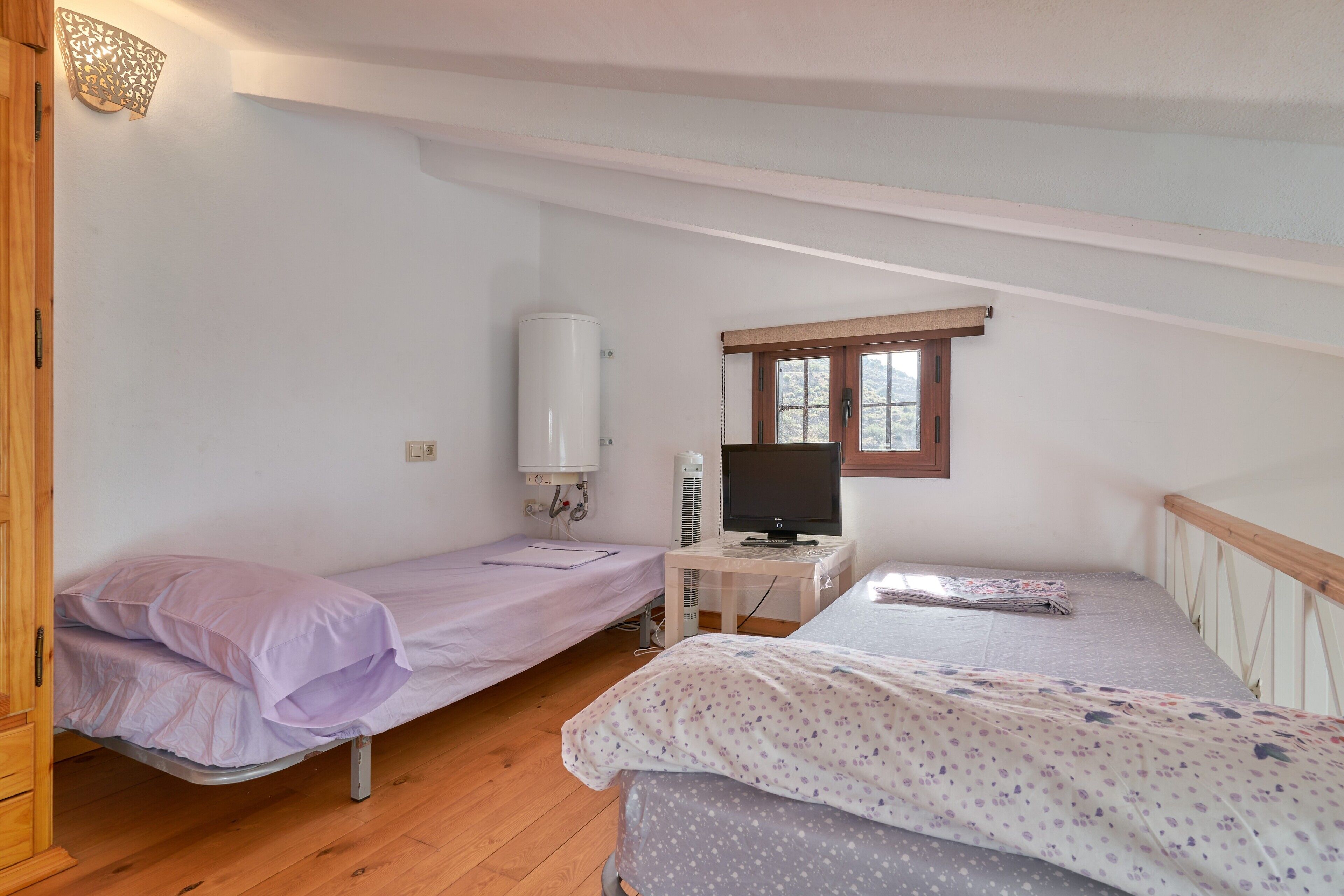 A dormitory room with two single beds, a desk with a computer, a heater, and a window.