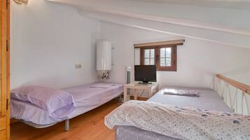 A dormitory room with two single beds, a desk with a computer, a heater, and a window.