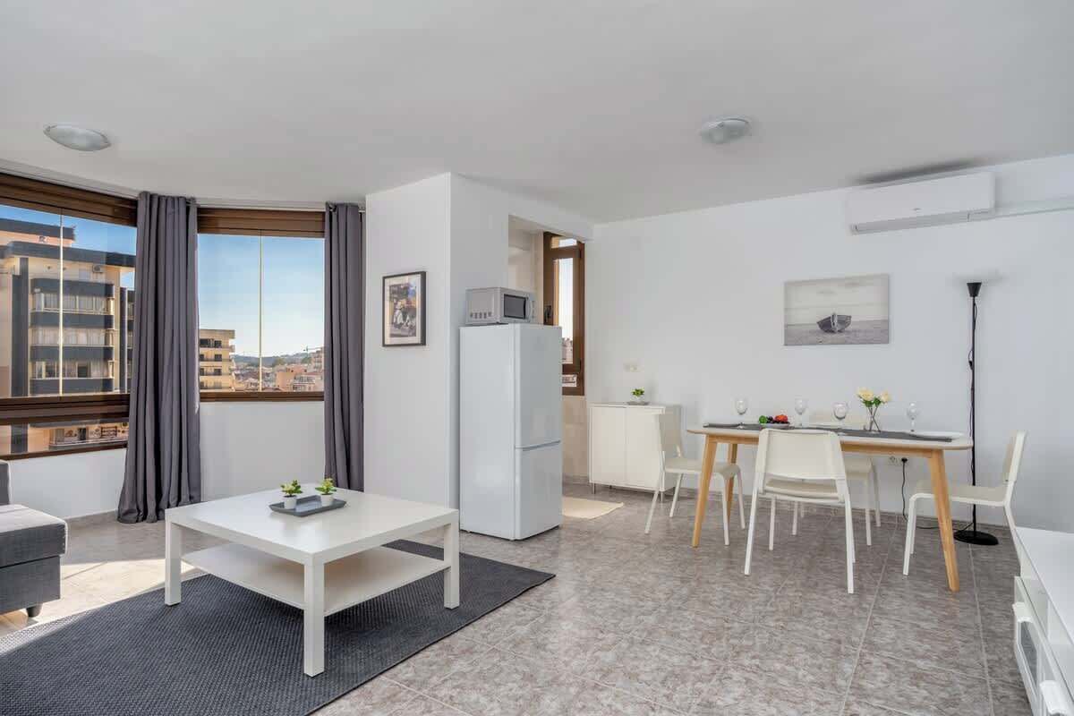 A modern, well-lit room with a dining area, a refrigerator, and a large window offering a city view.