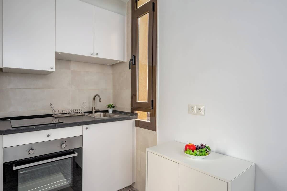 A kitchen with white cabinets, a black countertop, a stainless steel oven, a sink, and a small white cabinet with a fruit bowl.